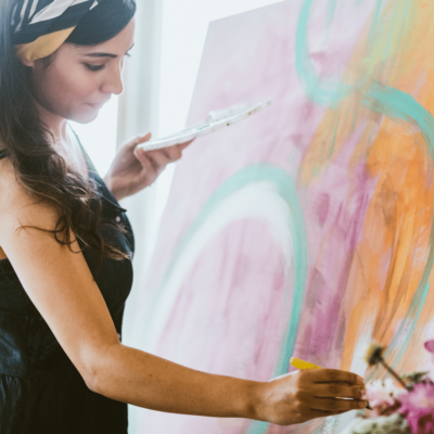 square image of a woman painting on a canvas with very colorful strokes